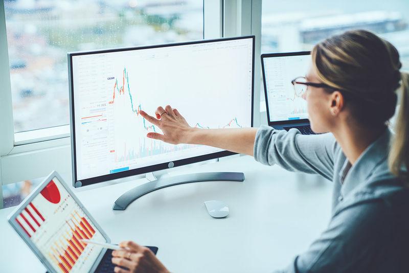 woman pointing to computer screen and tablet featuring bars and graphs