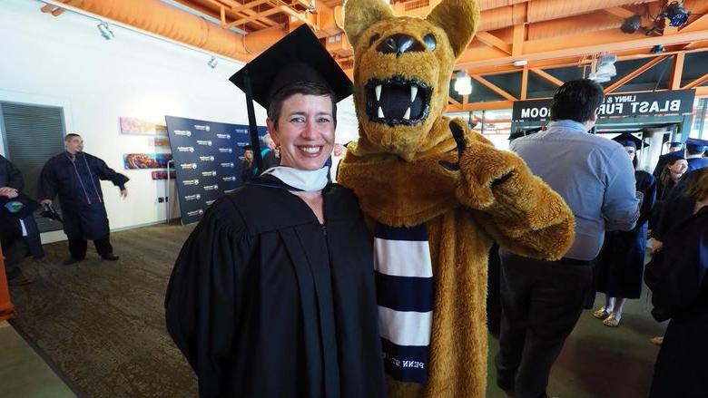 Nittany Lion posing with woman in cap and gown