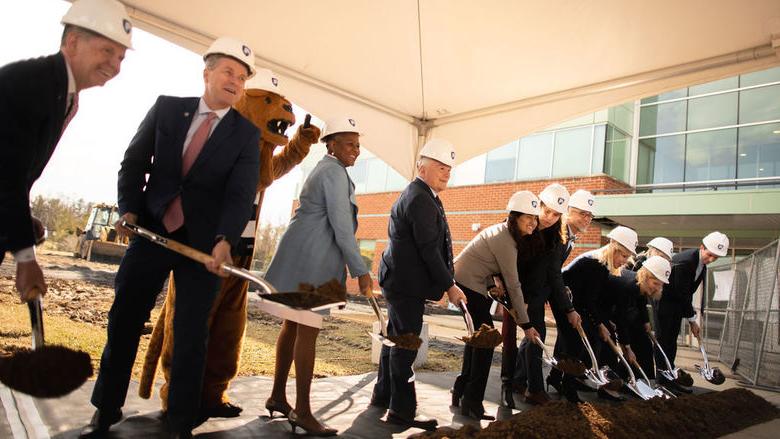 twelve people with shovels in hand turn over dirt