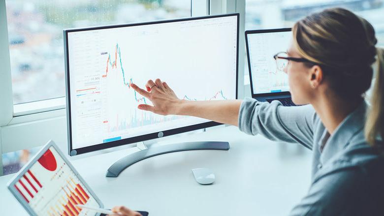 woman pointing to computer screen and tablet featuring bars and graphs