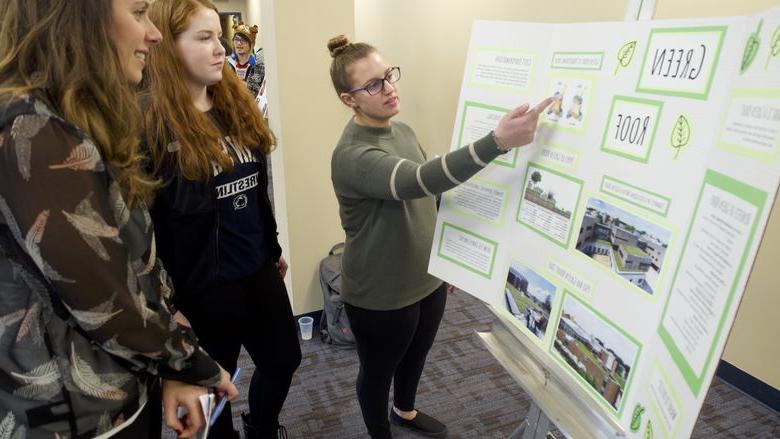 student pointing to a poster showing her research to bystanders