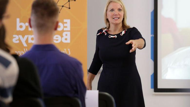 woman gesturing while speaking to a class of students