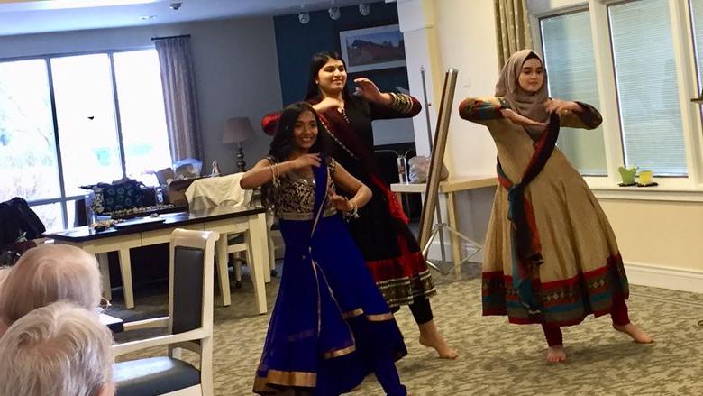 three young women in cultural dress dancing at senior center