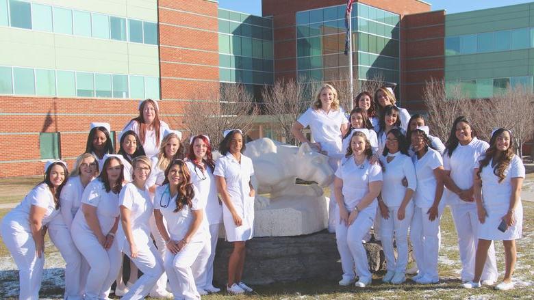 more than 20 women in white nursing outfits posing by Nittany Lion shrine statue